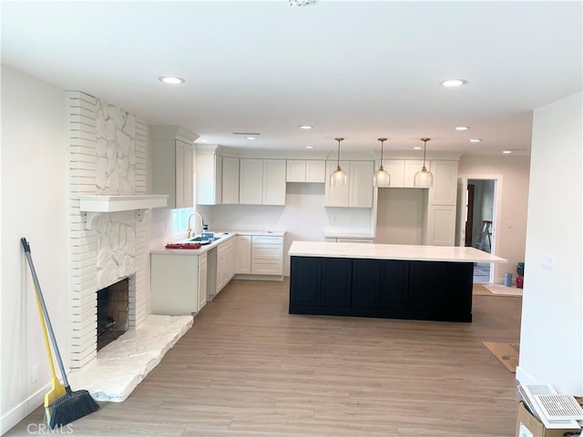 kitchen with a fireplace, white cabinets, hanging light fixtures, a center island, and light hardwood / wood-style floors