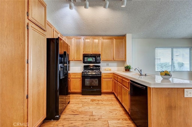 kitchen with black appliances, sink, tile counters, kitchen peninsula, and light hardwood / wood-style flooring