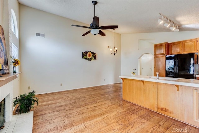 kitchen featuring light hardwood / wood-style flooring, a kitchen breakfast bar, a fireplace, black fridge with ice dispenser, and vaulted ceiling