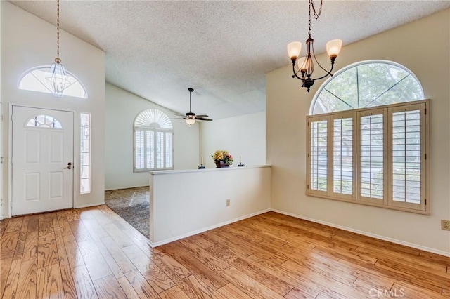 entrance foyer with ceiling fan with notable chandelier, plenty of natural light, a textured ceiling, and light wood-type flooring