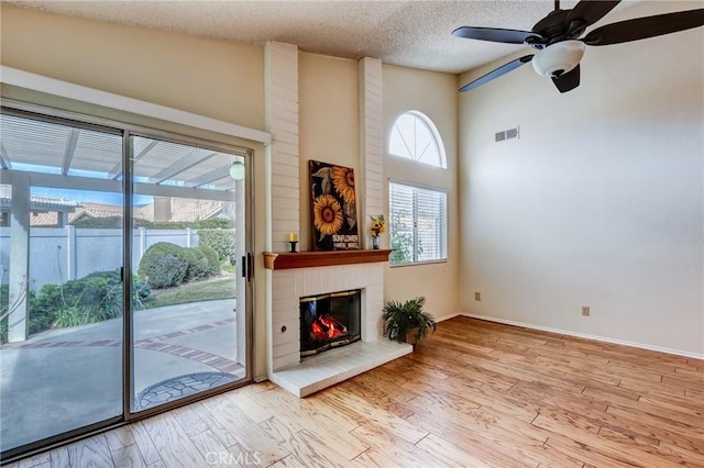 unfurnished living room featuring high vaulted ceiling, a brick fireplace, a textured ceiling, ceiling fan, and light hardwood / wood-style floors