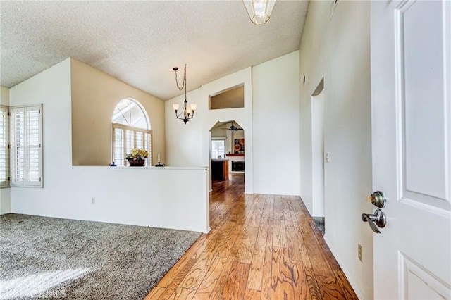 entrance foyer featuring an inviting chandelier, lofted ceiling, wood-type flooring, and a textured ceiling