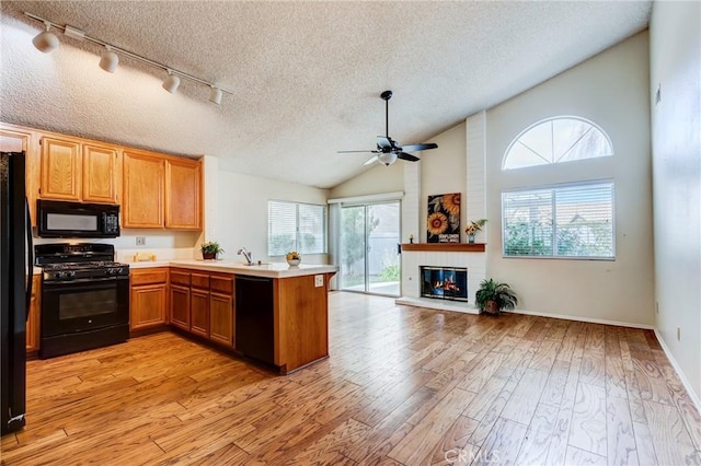 kitchen with black appliances, a textured ceiling, vaulted ceiling, kitchen peninsula, and light wood-type flooring