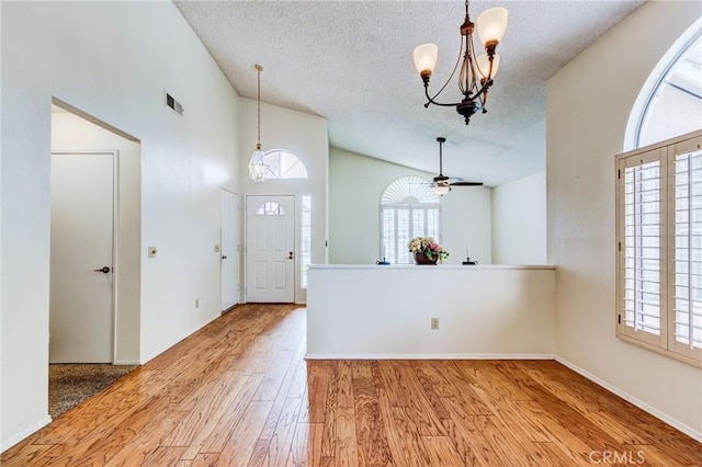 entrance foyer featuring hardwood / wood-style flooring, ceiling fan with notable chandelier, high vaulted ceiling, and a textured ceiling