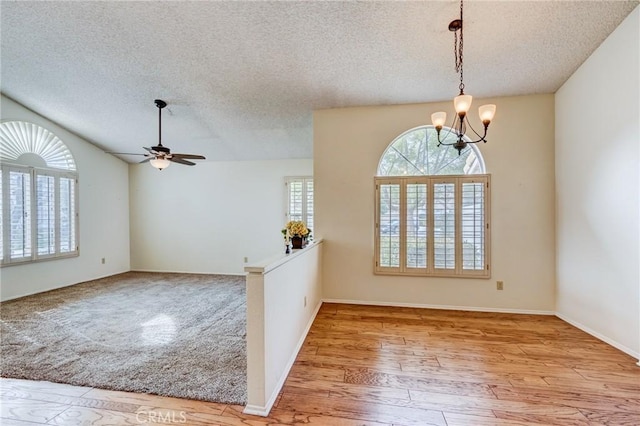 empty room with light wood-type flooring, ceiling fan with notable chandelier, and a textured ceiling