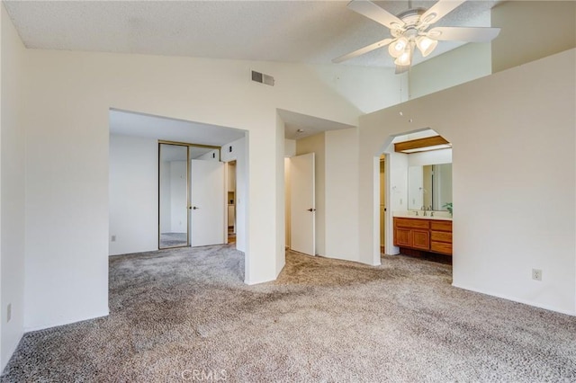 unfurnished bedroom with connected bathroom, high vaulted ceiling, light colored carpet, ceiling fan, and a closet