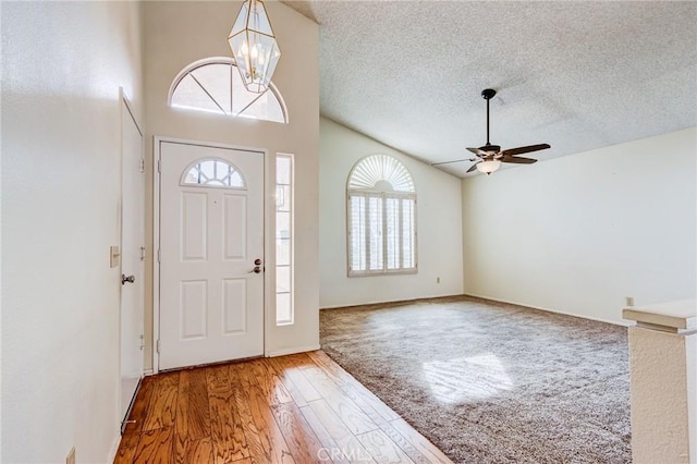 entrance foyer with hardwood / wood-style floors, ceiling fan with notable chandelier, high vaulted ceiling, and a textured ceiling