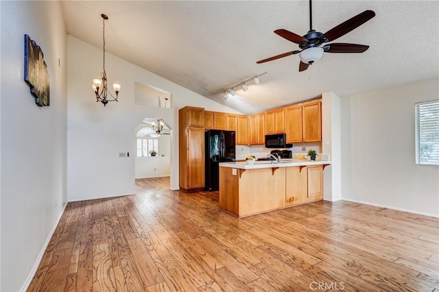 kitchen featuring decorative light fixtures, vaulted ceiling, light wood-type flooring, kitchen peninsula, and black appliances