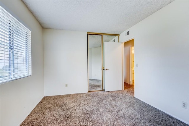 unfurnished bedroom with multiple windows, light colored carpet, a closet, and a textured ceiling