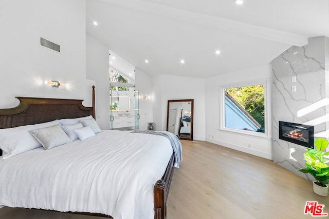 bedroom featuring a high end fireplace, light hardwood / wood-style flooring, and vaulted ceiling with beams