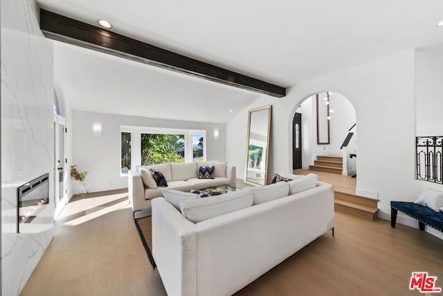 living room featuring lofted ceiling with beams, a premium fireplace, and light hardwood / wood-style floors