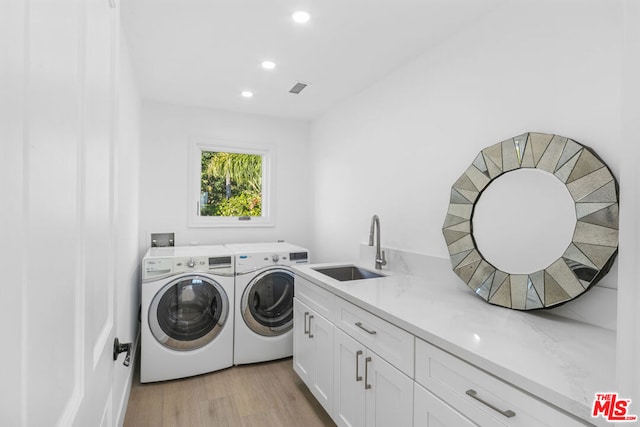 laundry area with cabinets, washing machine and clothes dryer, light hardwood / wood-style floors, and sink