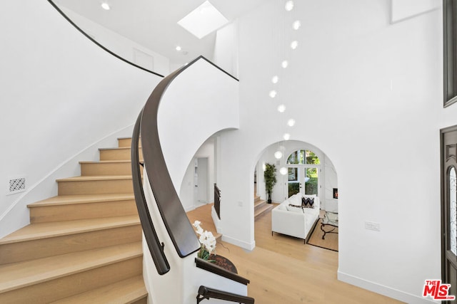 stairway with a towering ceiling, a skylight, and hardwood / wood-style floors