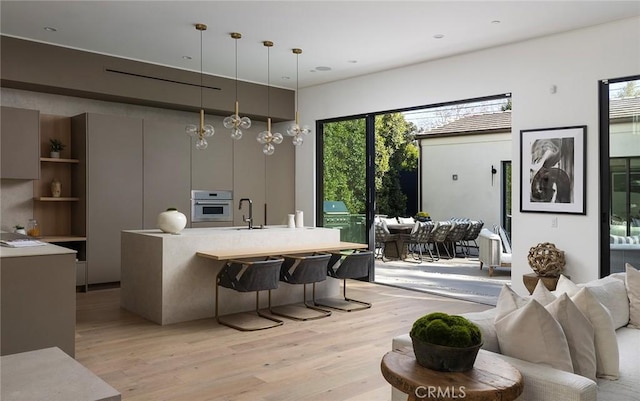 kitchen with sink, a breakfast bar area, decorative light fixtures, oven, and light wood-type flooring