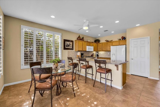 kitchen featuring light tile patterned flooring, a kitchen bar, white appliances, light stone countertops, and backsplash