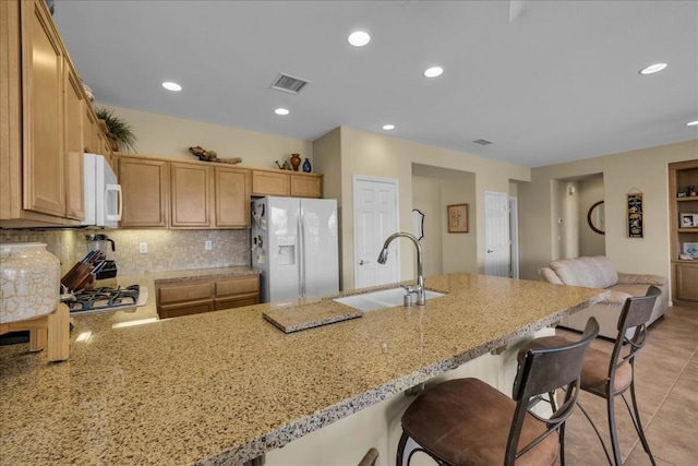 kitchen featuring sink, decorative backsplash, light stone counters, kitchen peninsula, and white appliances