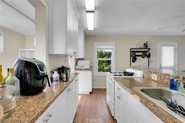 kitchen featuring white cabinetry, sink, a healthy amount of sunlight, white gas stove, and light wood-type flooring