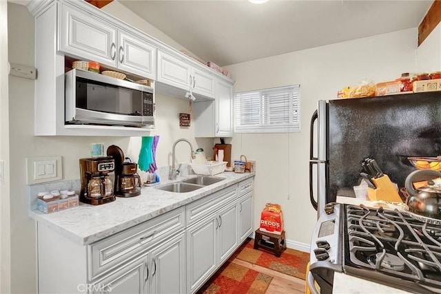 kitchen featuring sink, light tile patterned floors, appliances with stainless steel finishes, light stone counters, and white cabinets