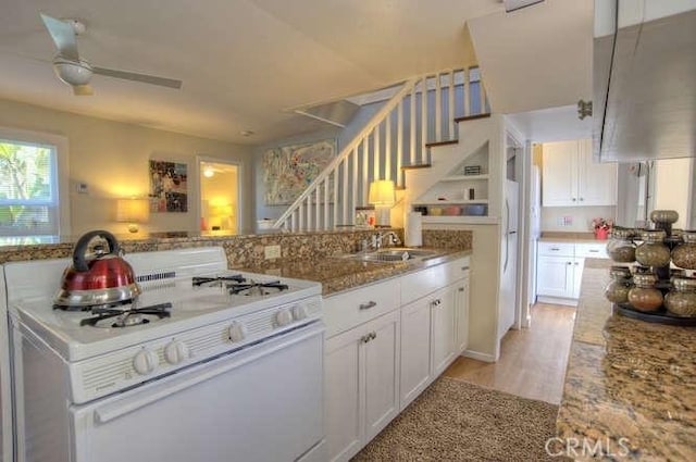 kitchen with white range with gas cooktop, sink, white cabinets, and light hardwood / wood-style floors