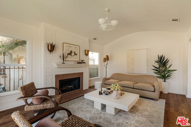 living room featuring a fireplace, dark wood-type flooring, vaulted ceiling, and a notable chandelier