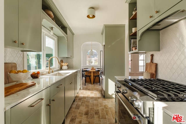 kitchen featuring sink, green cabinets, high end range, decorative backsplash, and decorative light fixtures