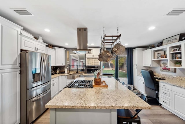 kitchen with a kitchen island, island range hood, built in desk, white cabinetry, and stainless steel appliances