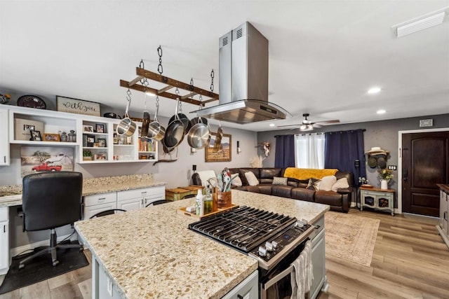 kitchen with stainless steel gas stove, white cabinetry, a center island, light stone countertops, and island exhaust hood