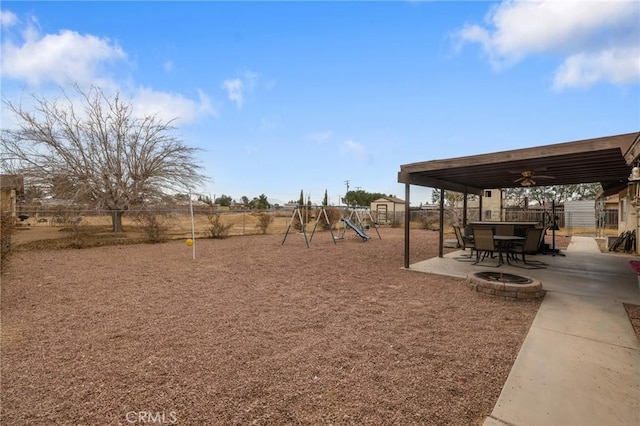 view of yard featuring ceiling fan, an outdoor fire pit, a playground, and a patio area