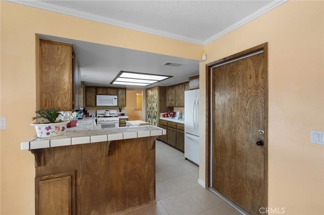 kitchen featuring a kitchen bar, tile countertops, ornamental molding, kitchen peninsula, and white appliances