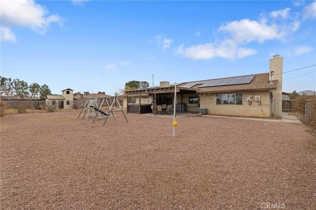 back of house featuring a playground, a patio area, and solar panels