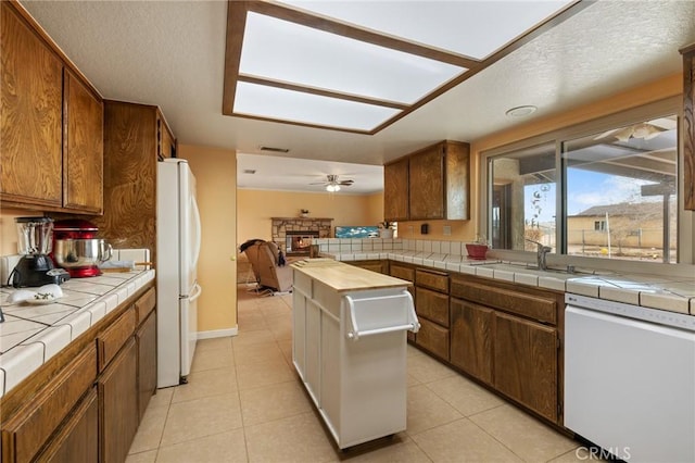 kitchen featuring a fireplace, sink, tile counters, ceiling fan, and white appliances