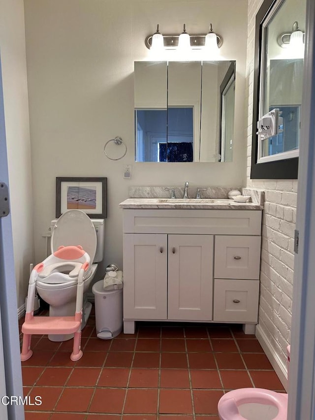 bathroom with vanity, tile patterned flooring, toilet, and brick wall