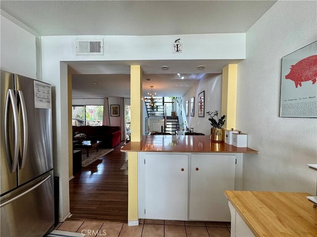 kitchen with light tile patterned floors, kitchen peninsula, stainless steel refrigerator, and white cabinets