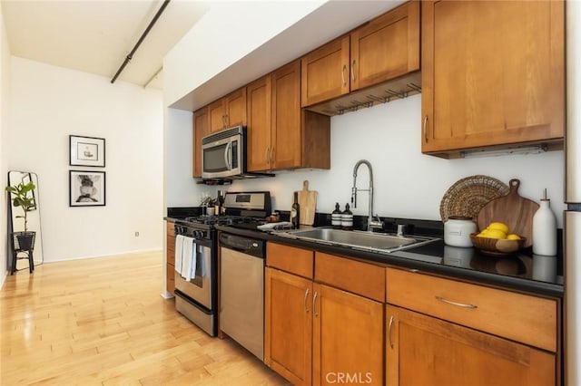 kitchen with appliances with stainless steel finishes, sink, and light hardwood / wood-style flooring