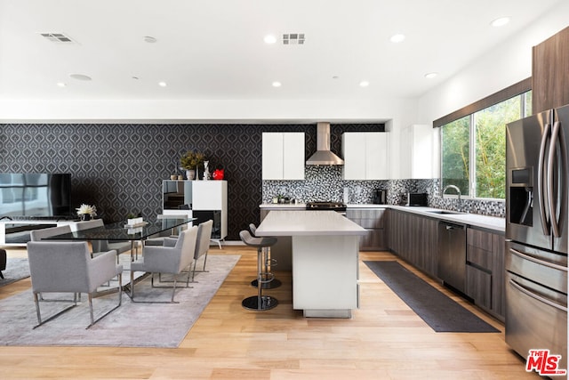 kitchen with wall chimney exhaust hood, a center island, dark brown cabinets, appliances with stainless steel finishes, and white cabinets