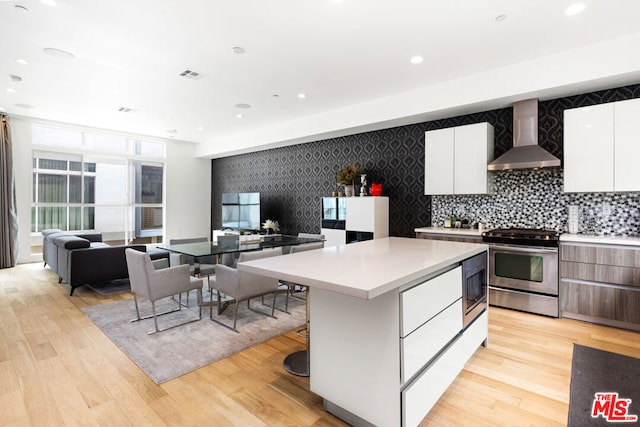 kitchen featuring wall chimney exhaust hood, a kitchen island, stainless steel appliances, light hardwood / wood-style floors, and white cabinets