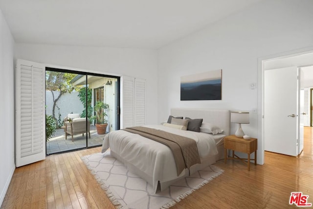 bedroom with wood-type flooring, vaulted ceiling, and access to outside