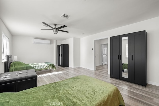 bedroom with a wall mounted air conditioner, ceiling fan, and light wood-type flooring