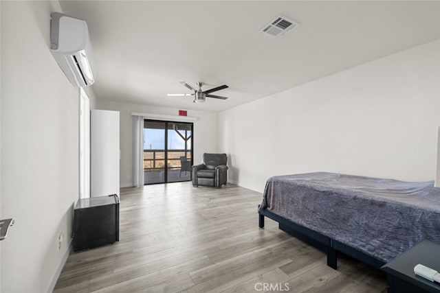 bedroom featuring hardwood / wood-style flooring, a wall mounted AC, and ceiling fan