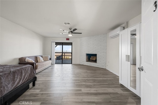 living room featuring an AC wall unit, dark wood-type flooring, ceiling fan, and a brick fireplace