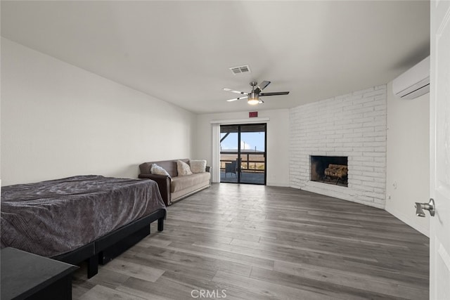 bedroom with an AC wall unit, hardwood / wood-style floors, ceiling fan, and a brick fireplace