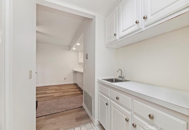 bar featuring white cabinetry, sink, and light hardwood / wood-style flooring