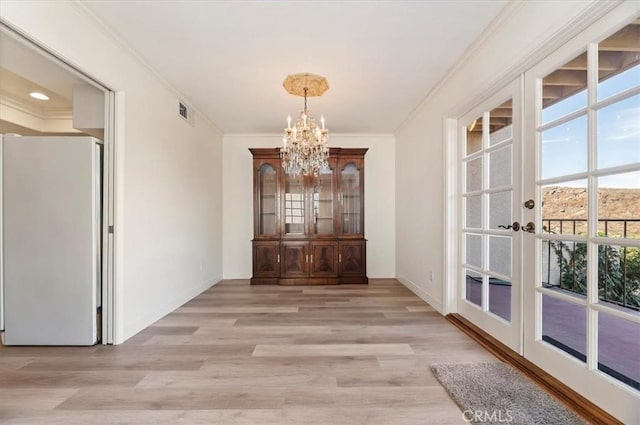 interior space featuring an inviting chandelier, light hardwood / wood-style flooring, ornamental molding, and french doors