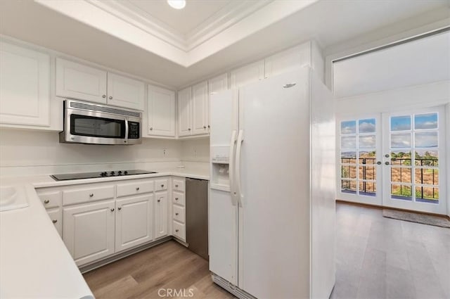 kitchen with crown molding, white cabinetry, a tray ceiling, light hardwood / wood-style floors, and white fridge with ice dispenser