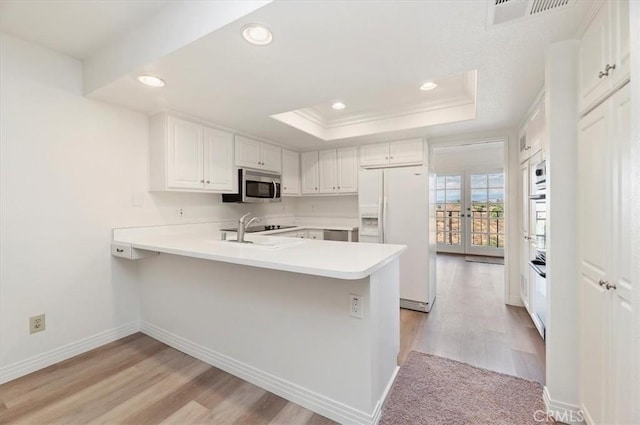 kitchen featuring white cabinetry, light hardwood / wood-style flooring, a tray ceiling, kitchen peninsula, and white refrigerator with ice dispenser