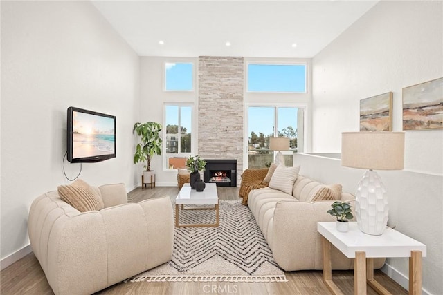 living room with a tiled fireplace, a towering ceiling, a wealth of natural light, and light hardwood / wood-style floors