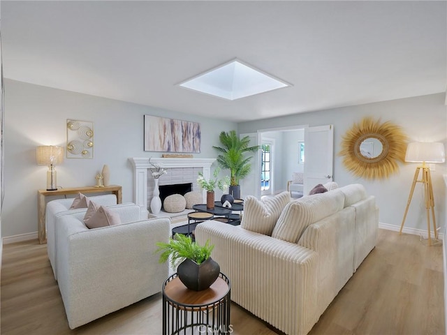 living room with a fireplace, a skylight, and light hardwood / wood-style floors