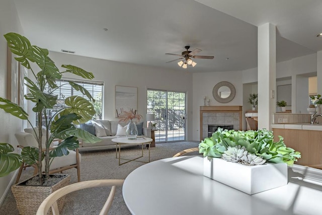 carpeted living room featuring a tiled fireplace and ceiling fan