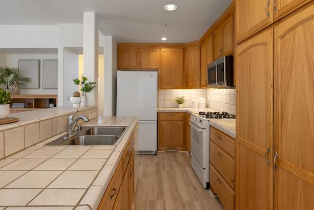 kitchen with tile countertops, sink, decorative backsplash, light hardwood / wood-style floors, and white appliances