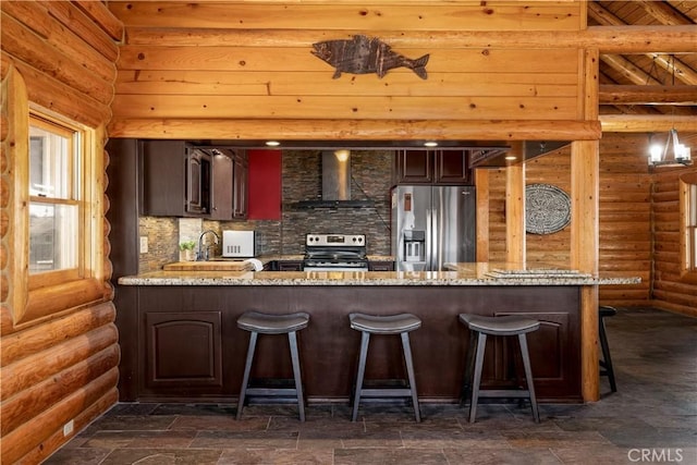 kitchen featuring a peninsula, stainless steel appliances, a sink, light stone counters, and wall chimney range hood